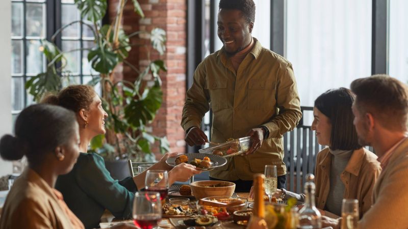 portrait-smiling-african-american-man-serving-food-while-hosting-dinner-party-with-friends-family-home